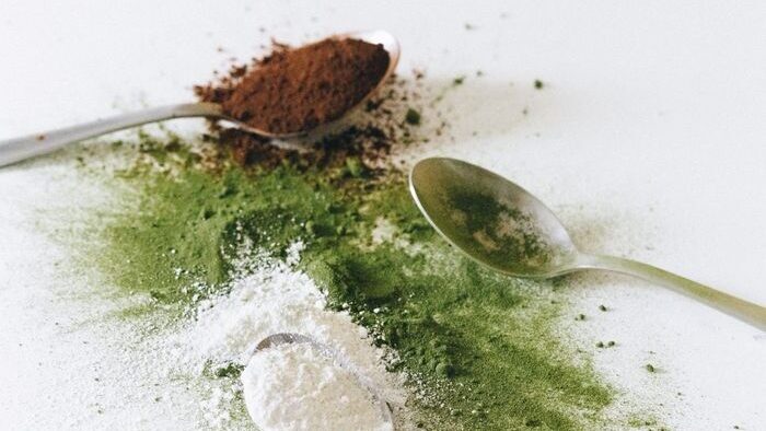 Close-up of assorted spices and powders with spoons on a white surface.