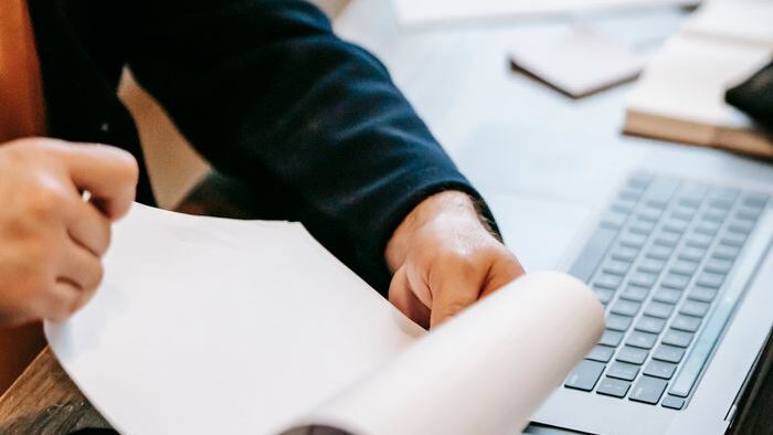 Person reviewing documents with laptop for work analysis.