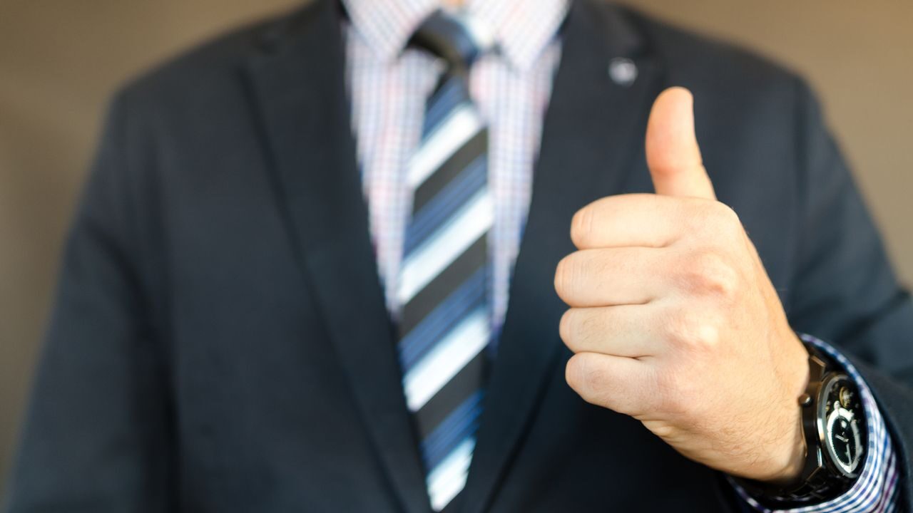 Close-up of a businessman in a suit giving a thumbs up gesture, symbolizing success.